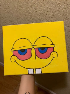 someone is holding up a yellow square with blue eyes and a smiley face on it