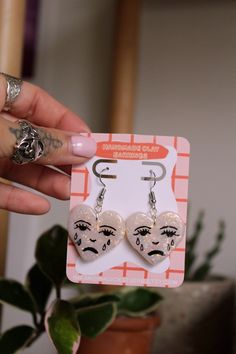 a pair of earrings with faces on them are being held up by a woman's hand