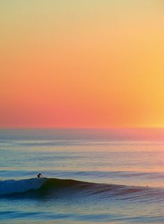 a person riding a wave on top of a surfboard in the ocean at sunset