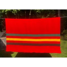 a red and grey striped blanket hanging on a clothes line in front of some trees