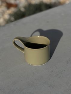 a coffee cup sitting on top of a cement table next to a shadow from the sun