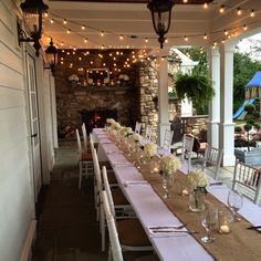 a long table set up with white flowers and candles on it for an outdoor event