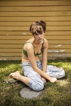 a young woman sitting on the ground in front of a house with her legs crossed