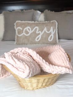 a basket that has some blankets in it on top of a bed next to pillows