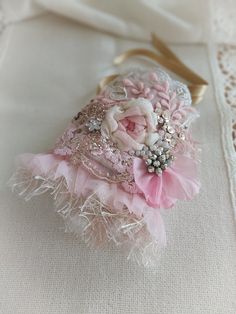 a pink and white flower brooch sitting on top of a lace covered table cloth