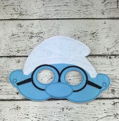 a blue and white felt mask with glasses on the face, sitting on a wooden surface