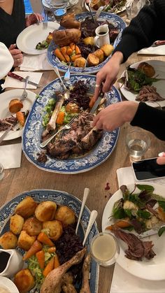 several people are serving themselves food at a long table with blue and white plates on it