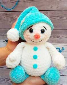 a hand holding a small white and blue snowman stuffed animal in it's left hand