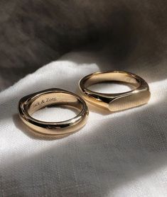 two gold wedding rings sitting on top of a white cloth