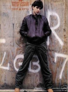 a young man standing in front of a wooden wall with graffiti on it's side