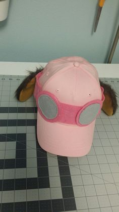 a pink hat with goggles on it sitting on top of a tiled floor next to scissors