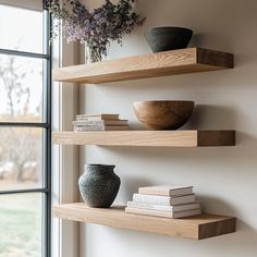 three wooden shelves with vases and books on them in front of a large window