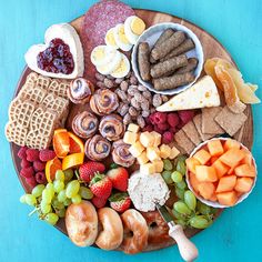 a platter filled with meats, fruit and crackers on a blue table