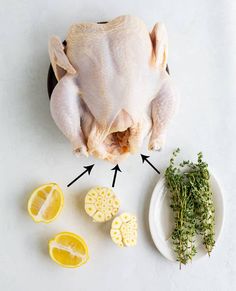 a whole chicken sitting on top of a table next to sliced lemons and herbs