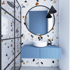 a bathroom with blue cabinets and a round mirror on the wall above it is decorated with geometric shapes