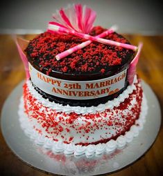 a red and white cake on a plate with pink ribbon around it that says happy 25th marriage anniversary