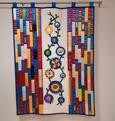 a quilt hanging on the wall with flowers and ribbons attached to it's sides