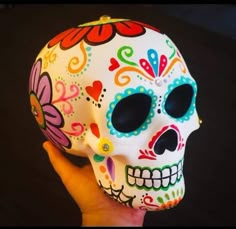 a hand holding a colorful skull with flowers on it