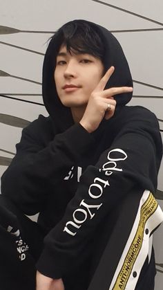 a young man wearing a black hoodie pointing to the left with his finger up