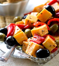 a glass dish filled with olives, peppers and cheese