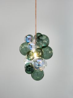 a green and clear light hanging from a wooden cord in front of a white wall