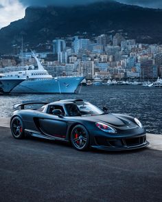 a black sports car parked in front of a large body of water with a cruise ship in the background