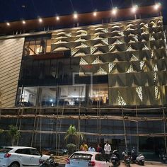 some cars parked in front of a building with scaffolding on the side and lights above it