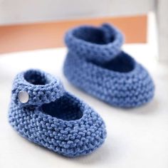 two crocheted blue baby shoes sitting on top of a white table next to a rocking chair