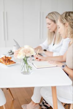 two women sitting at a white table writing