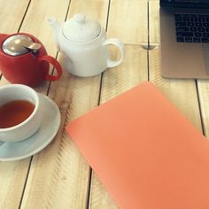 a laptop computer sitting on top of a wooden table next to a cup of tea