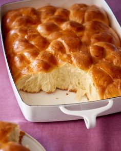 a baked pastry in a white dish on a purple table cloth next to plates and utensils