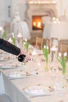 a person pouring wine into a glass at a table set with white plates and silverware