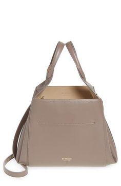 The label's favored trapezoidal silhouette defines a bucket bag crafted from ash-colored leather with a gold-foil logo and drawstring-cinched closure. Drawstring closure Top carry handles; removable, adjustable shoulder strap Structured silhouette with flat base for stability Lined Leather Made in Italy Designer Handbags Black Owned/Founded Tan Top Handle Bucket Bag With Gold-tone Hardware, Chic Tan Bucket Bag With Removable Pouch, Modern Tan Top Handle Bucket Bag, Chic Taupe Leather Bucket Bag, Modern Tan Bucket Bag With Removable Pouch, Gold Foil Logo, Handbags Black, Drawstring Top, Ash Brown