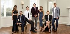 a group of people standing and sitting on chairs in a living room with hardwood floors