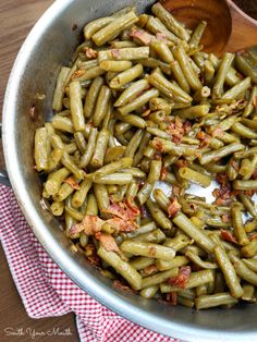 cooked green beans with bacon in a skillet on a wooden table top next to a red and white checkered napkin