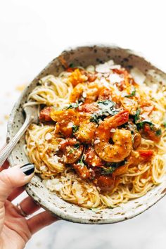 a person holding a bowl of pasta with shrimp and tomato sauce on it, ready to eat