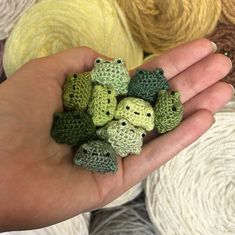 a hand holding small crocheted animals in front of balls of yarn