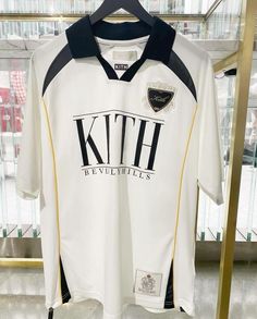 a white and black shirt hanging on a metal rack in front of a glass case