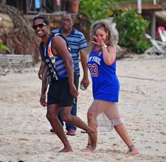 two men and a woman are walking on the beach while talking on their cell phones