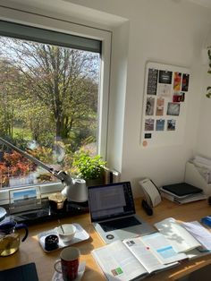 an open laptop computer sitting on top of a wooden desk next to a large window