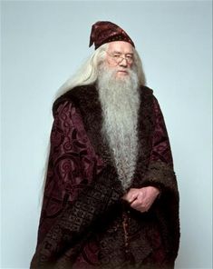 an old man with a long white beard wearing a red cape and black cloak, standing in front of a gray background