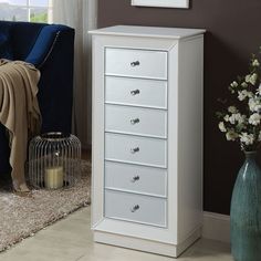 a white chest of drawers next to a blue chair and vase with flowers in it