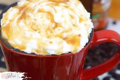 a red cup filled with whipped cream on top of coffee beans and caramel syrup