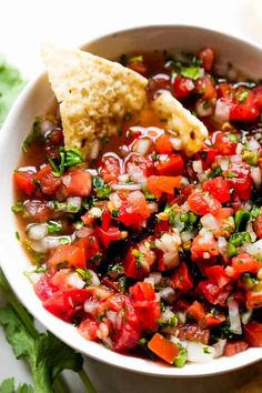 a white bowl filled with salsa and tortilla chips next to cilantro