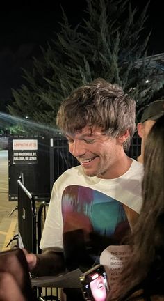 a man in a white t - shirt is smiling and looking at his cell phone