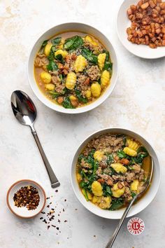 Two bowls of soup featuring gnocchi, Italian sausage, spinach, and croutons, accompanied by a spoon and chili flakes on the side.