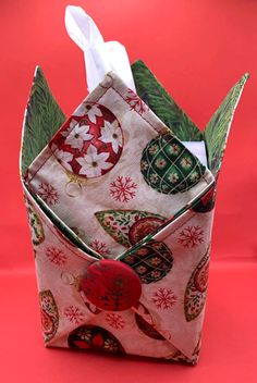 an origami box with tissue paper in it on a red surface, decorated with christmas ornaments