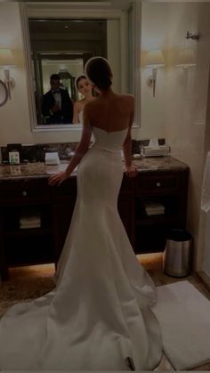 a woman standing in front of a bathroom mirror wearing a wedding dress and looking at herself in the mirror