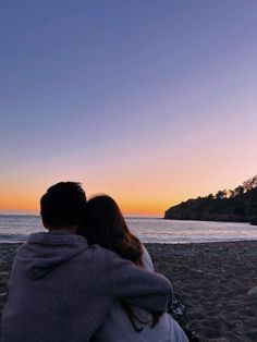 two people sitting on the beach watching the sunset