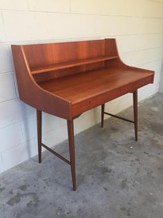 a wooden desk sitting in front of a white brick wall on concrete floored area